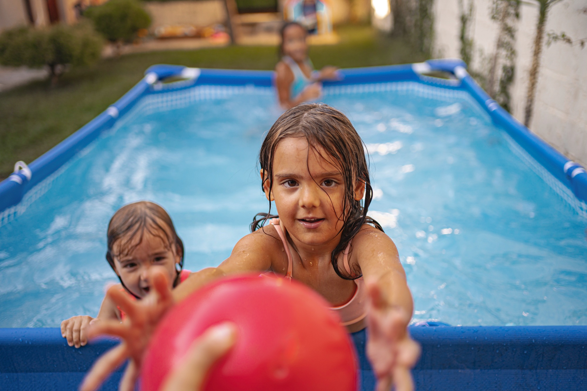 Children playing games with a red ball in an above-ground pool