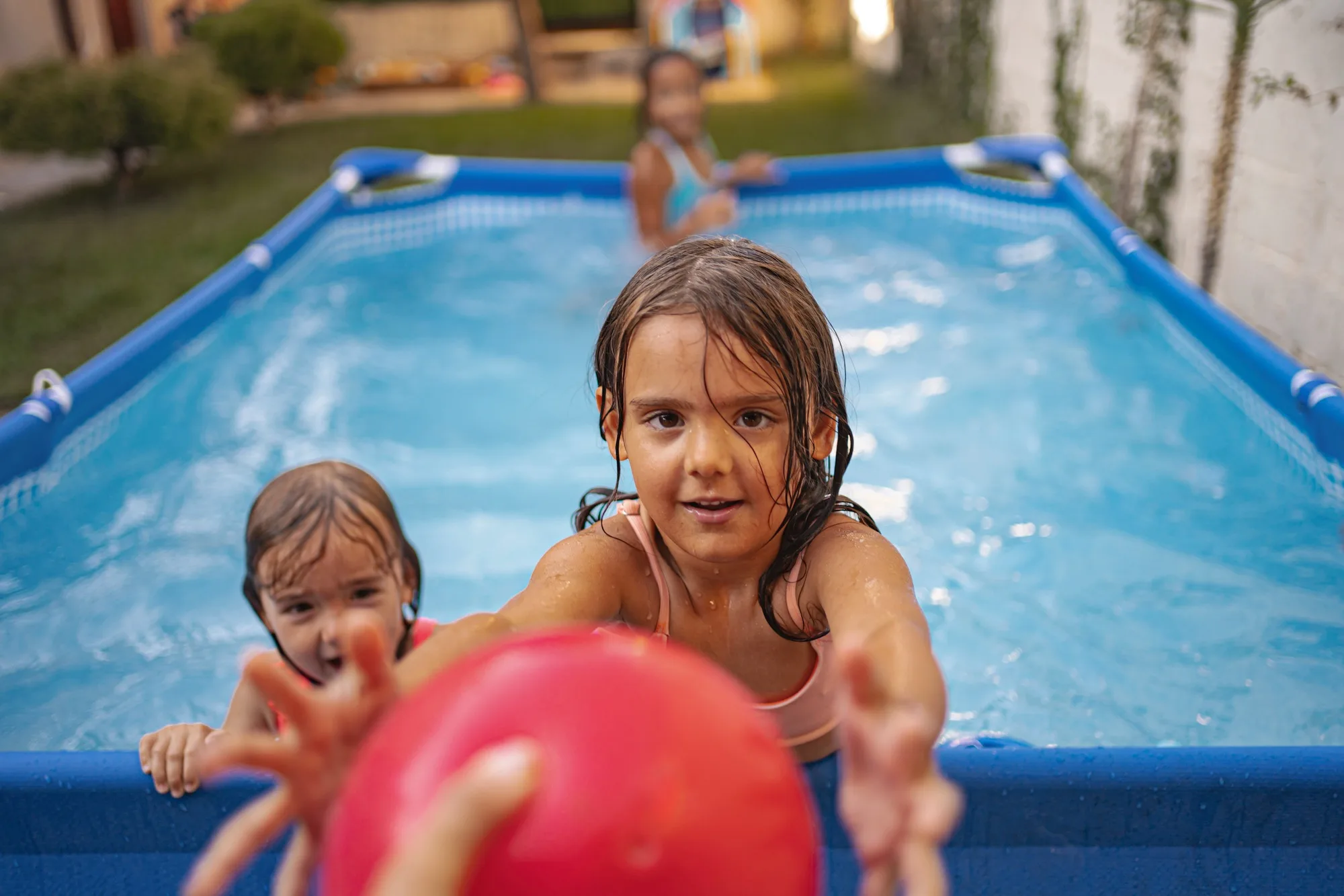 Children playing games with a red ball in an above-ground pool