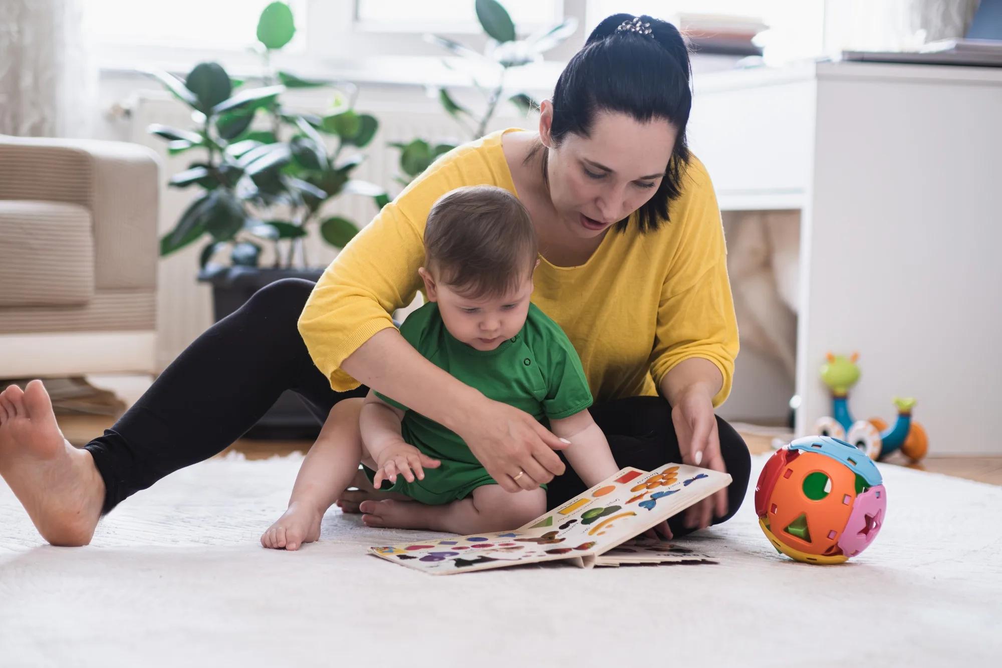 Focused mother showing little son interesting book with colorful pictures of animals