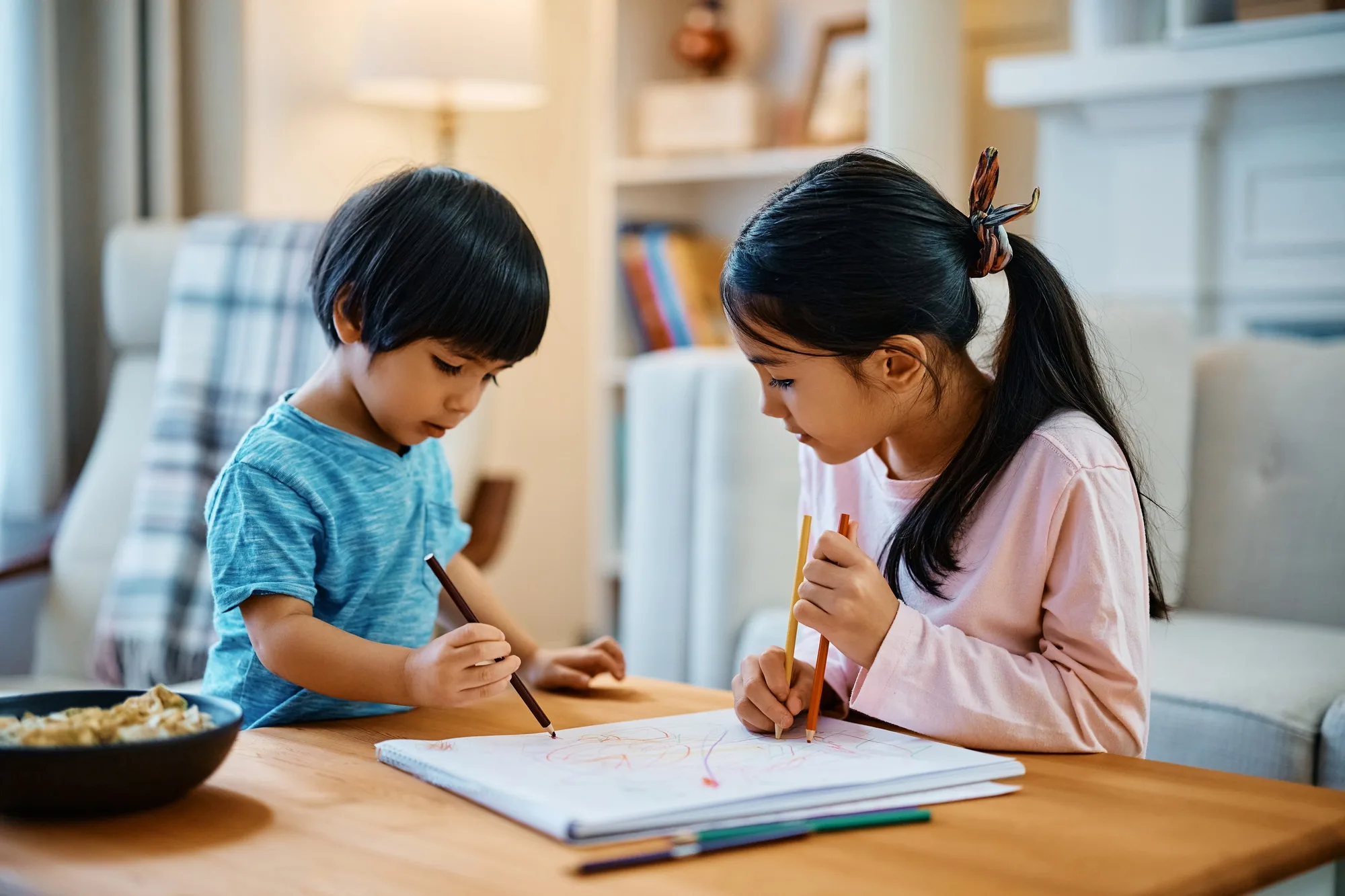 Little Asian boy enjoying in coloring on the paper with his sister at home.